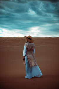 Rear view of woman standing at sandy beach against sky