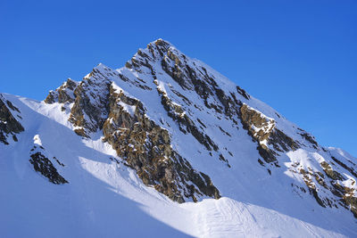 Low angle view of snowcapped mountains against clear blue sky