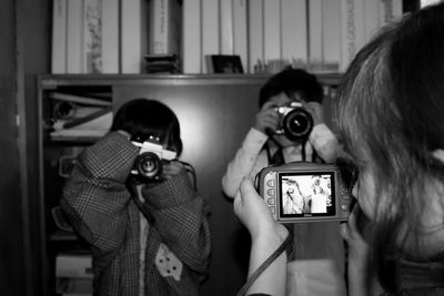 Girl photographing boys using cameras at home