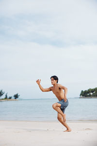 Full length of woman jumping at beach against sky