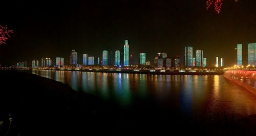 Illuminated buildings by river against sky at night