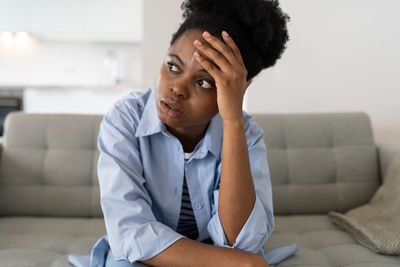 Flustered african american woman is very nervous sighing and touching face with hands sits on sofa