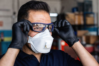 Adult man in latex gloves and respirator putting on protective goggles and looking at camera during work in garage