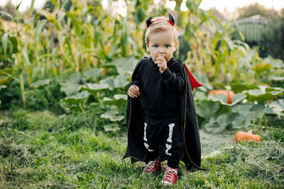 A kid in a carnival devil costume with pumpkins in the garden. halloween costume, tradition