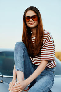Portrait of young woman sitting against car