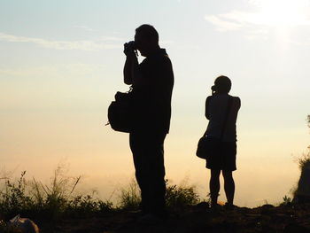 Silhouette couple standing on landscape against sky during sunset