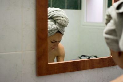 Reflection of woman with towel on mirror in bathroom