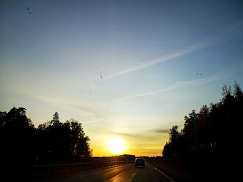 Silhouette trees by road against sky during sunset