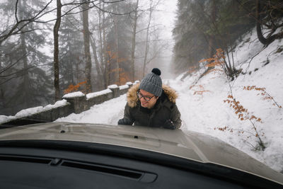 Man pushing car on snow covered road in forest