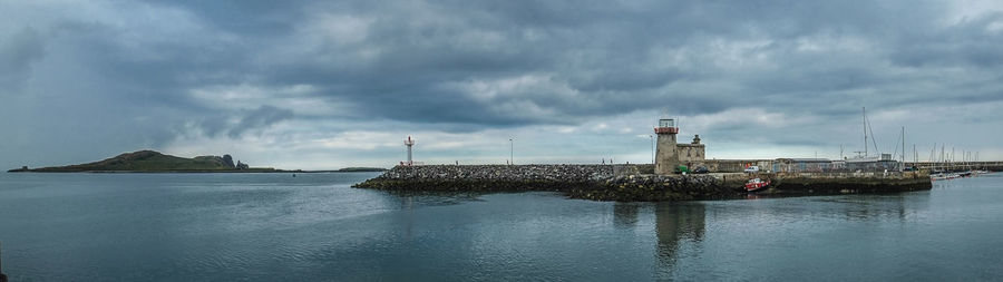 View of lighthouse by calm sea against cloudy sky