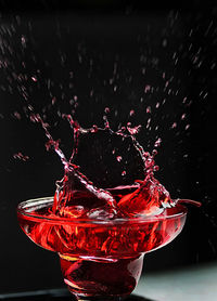 Close-up of red water splashing in glass against black background