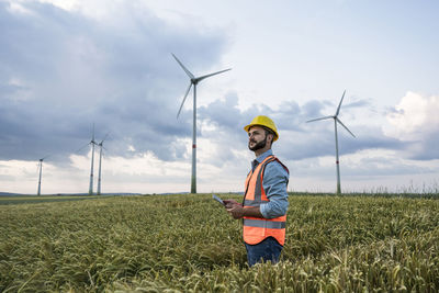 Engineer with tablet pc standing in field with wind turbines in background