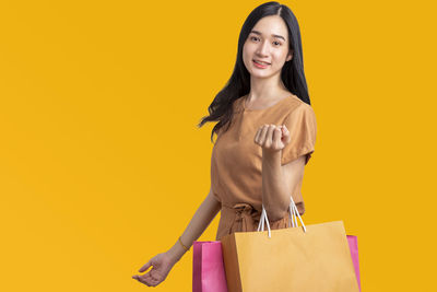 Portrait of young woman standing against yellow background