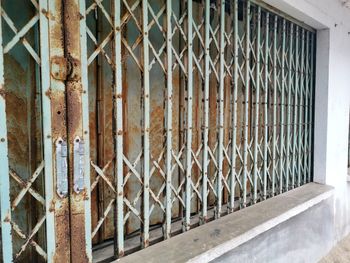 Close-up of rusty metal fence against abandoned building