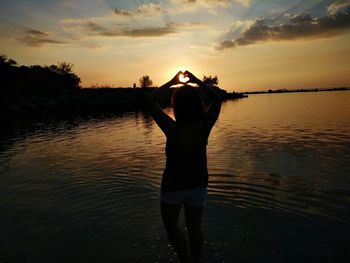 Rear view of silhouette woman standing in water at sunset