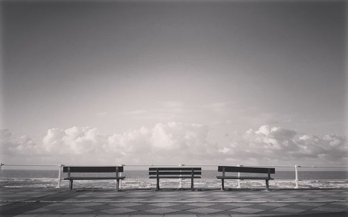 Empty bench on beach against sky