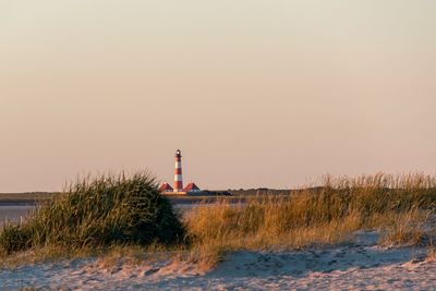 Lighthouse by sea against sky during sunset