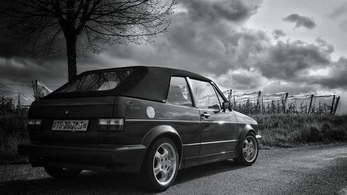 Cars parked on field against cloudy sky