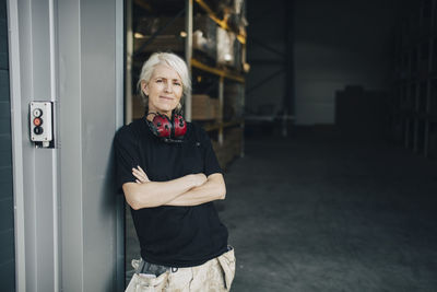 Smiling worker standing with arms crossed at entrance of industry