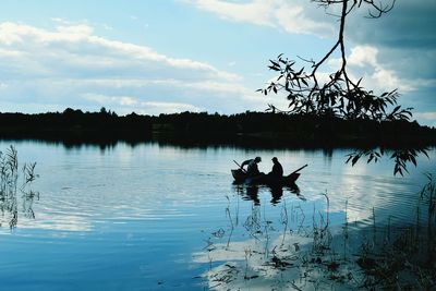 Silhouette fishermen in boat on lake against sky