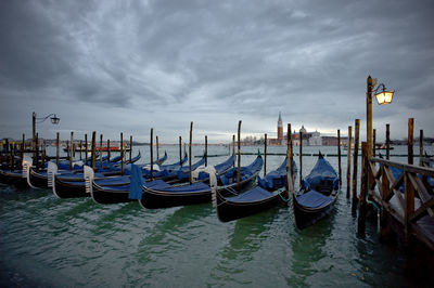 Gondolas moored at grand canal by santa maria della salute against cloudy sky