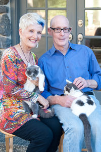 Portrait of senior couple holding cats while sitting at patio