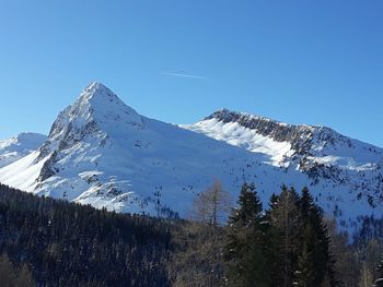 Low angle view of snowcapped mountains against clear blue sky