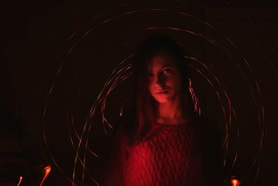 Portrait of young woman against light painting at night