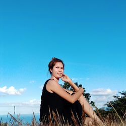 Portrait of young woman standing against blue sky