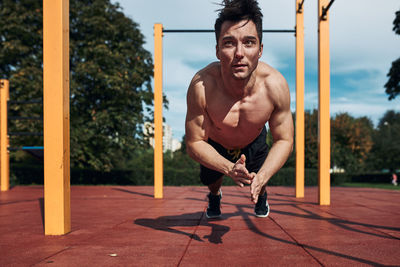 Young shirtless man bodybuilder doing clapping push-ups on a red rubber ground during his workout