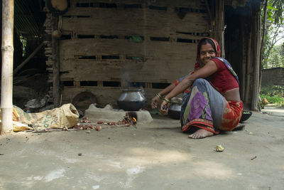 Full length of indian woman sitting outdoors making food on chulha