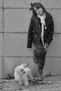 Portrait of girl with dog standing on footpath against wall