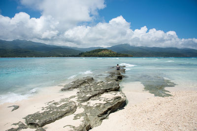 Rear view of woman sitting on rock at beach against sky