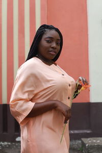 Portrait of young woman standing on road against wall