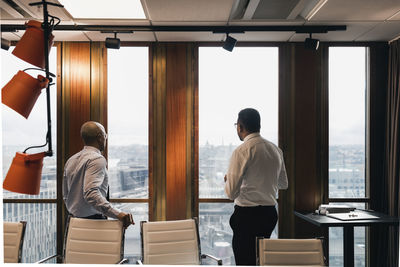 Male entrepreneurs looking through window while planning strategy in board room during meeting