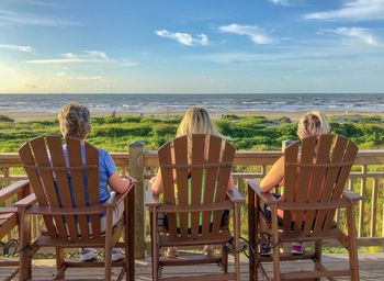 Rear view of people sitting on chair at beach against sky