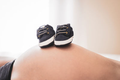 Midsection of pregnant woman with baby shoes on top at home