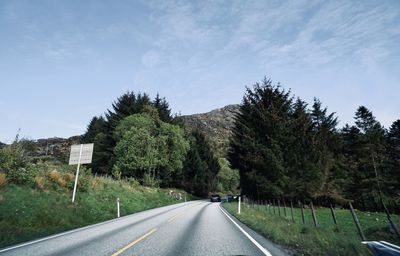 Country road by trees against sky