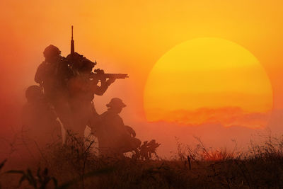 Silhouette men on field against orange sky