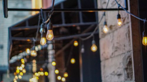 Low angle view of illuminated light bulbs hanging on building at night