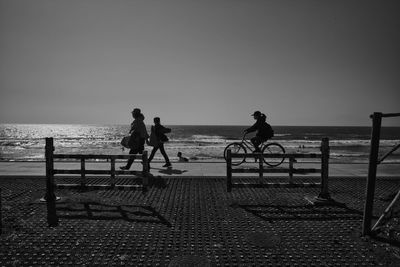 People riding bicycle on beach against clear sky