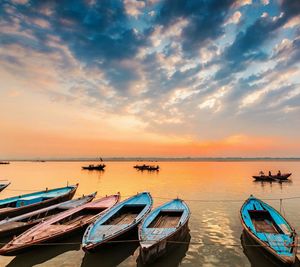 Rowboats moored in river against sky during sunset