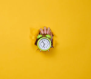 A woman's hand holds a round green alarm clock, the time is five minutes to seven in the morning. 