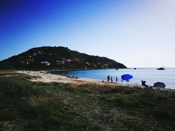 People on beach against clear blue sky