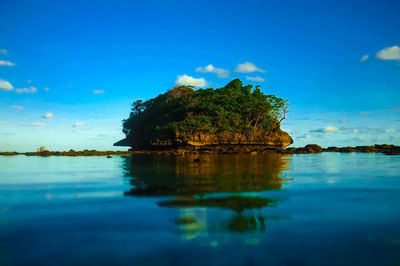 Reflection of rock in sea against blue sky