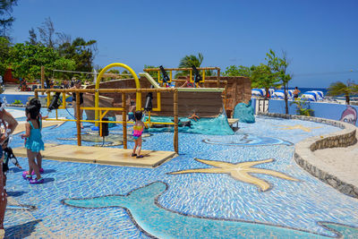 People playing in swimming pool against blue sky