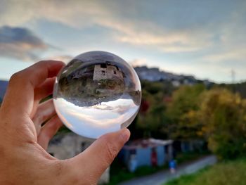 Close-up of person holding glass of crystal ball against sky