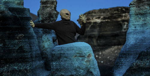 Man wearing alien mask standing by rock formation