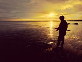 Rear view of man standing at beach against sky during sunrise