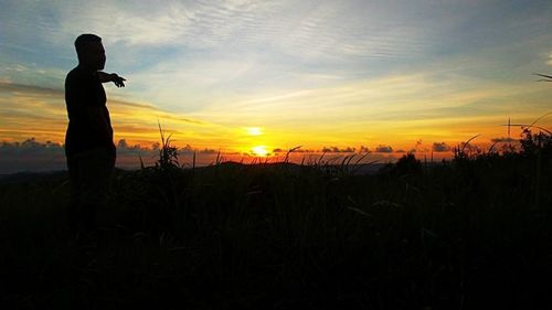 Silhouette man standing on field against sky during sunset